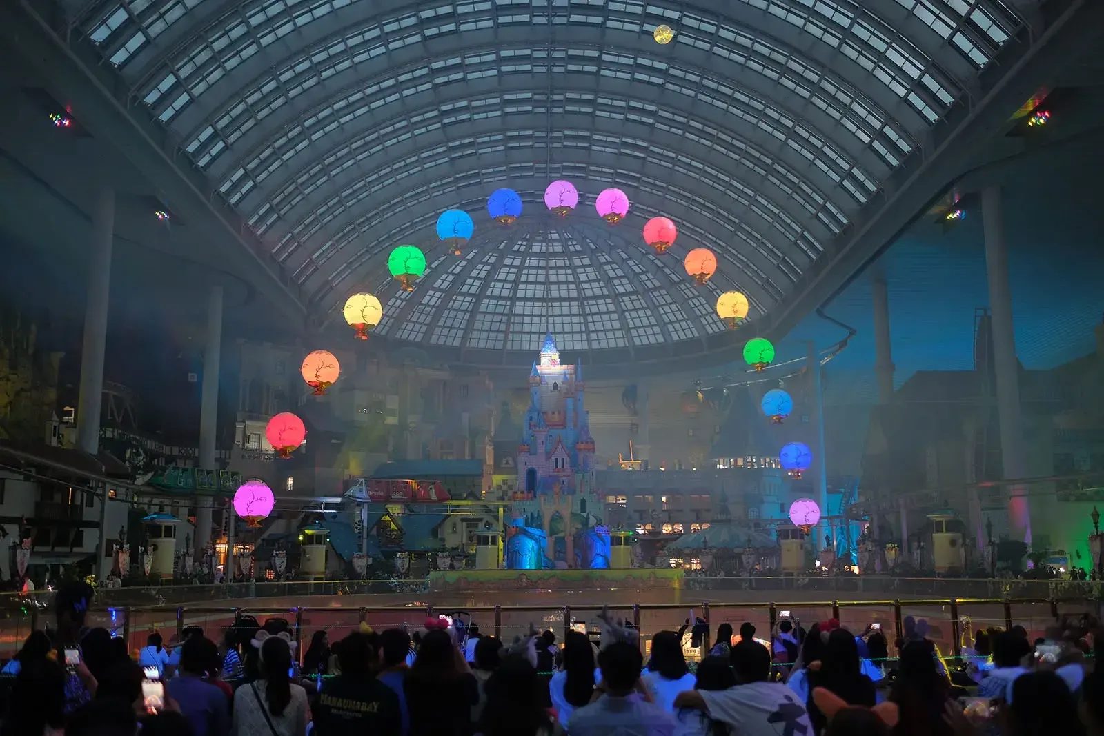 Colourful flying lanterns forming a rainbow arc under the glass dome of Lotte World Adventure